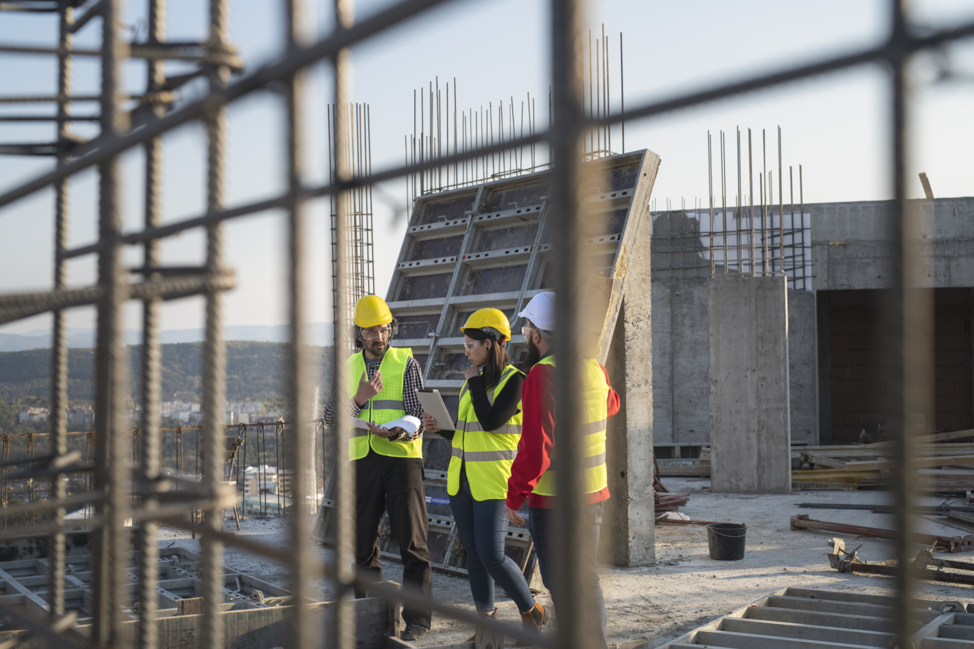 Construction workers standing on top level of partially constructed building reviewing building plans