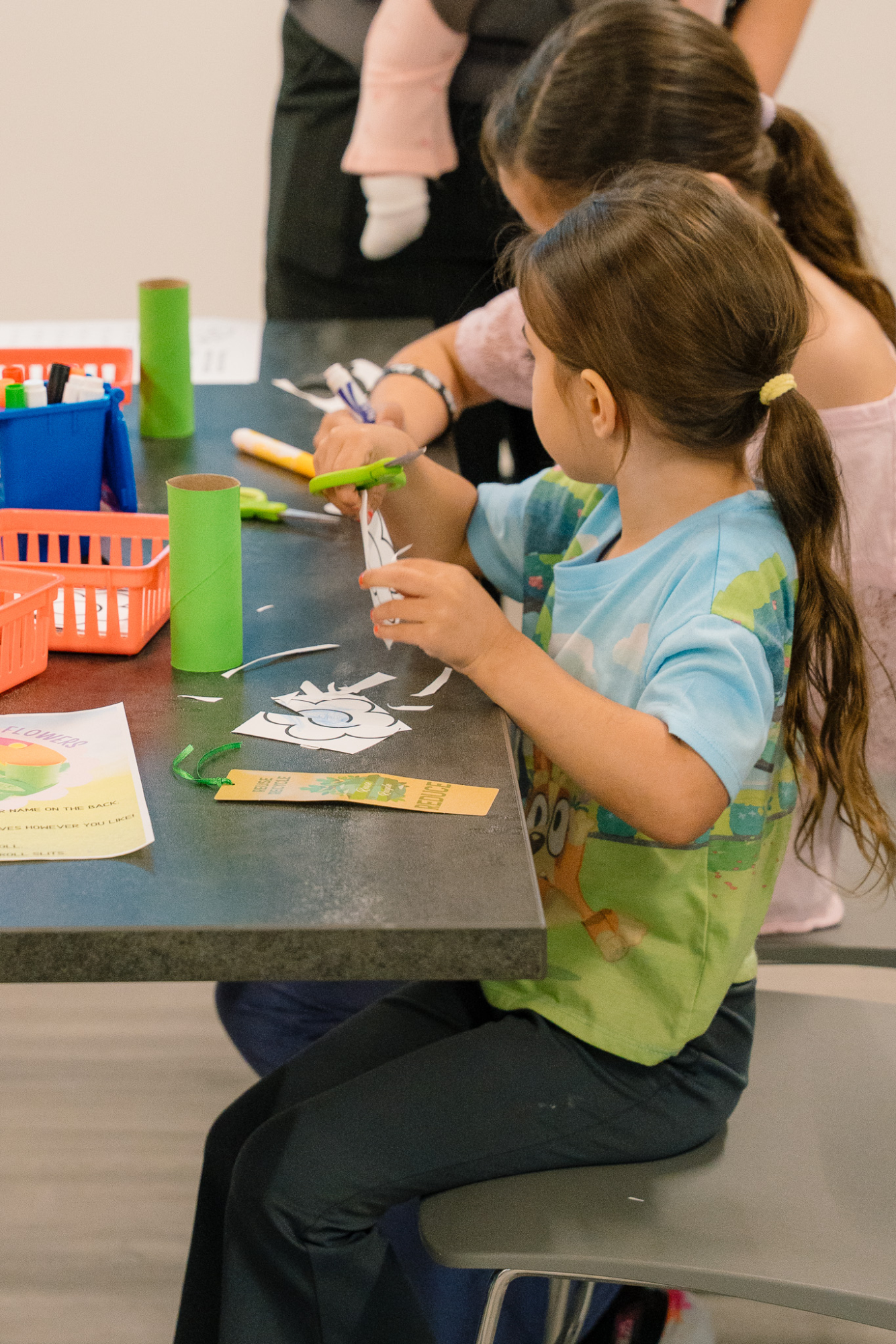 two children sit at a table cutting paper with scissors